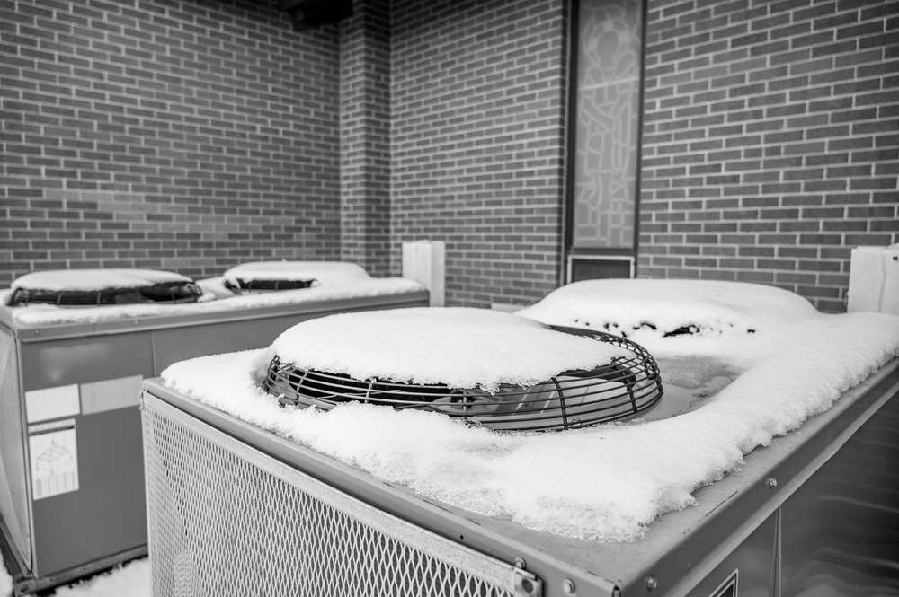 Outdoor mechanical air conditioning units idling during the winter with snow on top of the fans